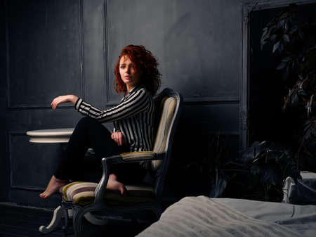 Ginger girl sitting at home on the design chair next to the tableの写真素材