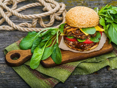 Big tasty hamburger with spices and herbs on wooden board and on tableの写真素材
