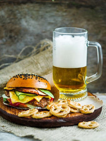 Tasty fresh hamburger with glass of beer and marinated cucumbers on wooden boardの写真素材