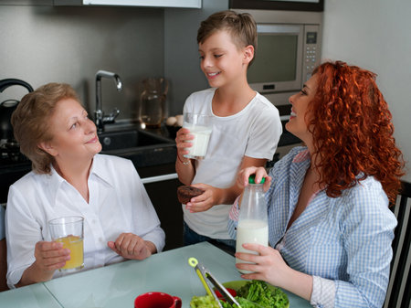 Happy granny drinking juice with children in the kitchen