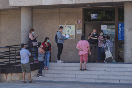 Madrid / Spain - 06/18/2020: Group of people waiting outside in public building. New situation in Spain about the pandemic of Covid-19. People are using mask in their new life routine.のeditorial素材