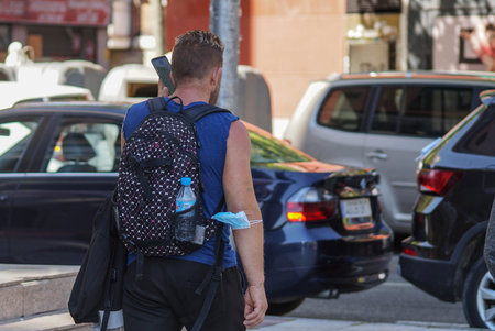 Madrid / Spain - 06/18/2020: Man walking with a mask in his elbow and using phone. New situation in...