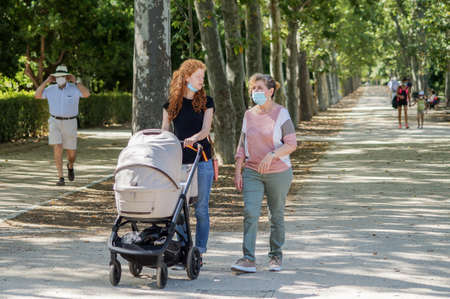 Madrid / Spain - 07 23 20: Mum is speaking with a friend in Retiro park with her buggy in the summer and using face maskのeditorial素材