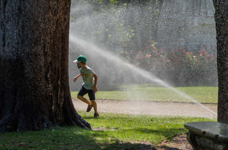 Madrid / Spain - 07 23 20: child running between sprinklers and playing with water in the summer at Retiro parkのeditorial素材