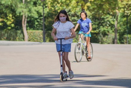 Madrid / Spain - 07 23 20: Kid with her scooter an Retiro park using a beautiful face mask in the summerのeditorial素材