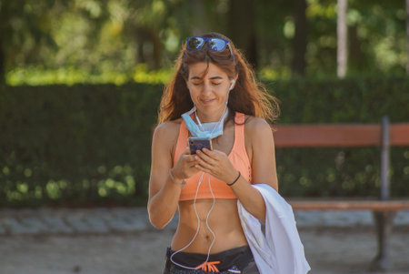 Madrid / Spain - 07 23 20: Close-up woman at Retiro park is using her mobile phone and wearing her face mask over the chinのeditorial素材