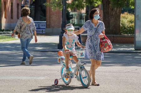 Madrid / Spain - 07 23 20: Two people, mum and daughter in Retiro park using face mask in the summer. The kid is with her bikeのeditorial素材