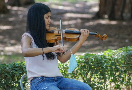 Madrid / Spain - 07 23 20: one young girl playing the violin on Retiro Park in the summer, with her...