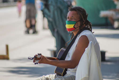 Madrid / Spain - 07 23 20: Musician playing guitar at Retiro park and wearing beautiful reggae mask with green, yellow and red colorsのeditorial素材
