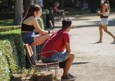 Madrid / Spain - 07 23 20: Two young people sitting on a bench in the summer, in Retiro park and not using face maskのeditorial素材