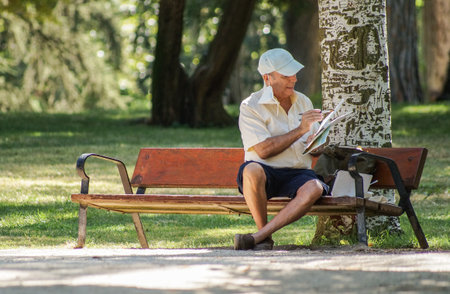 Madrid / Spain - 07 23 20: One artist sitting on a bench in Retiro park in the summer and painting in a paper. His face mask is on his ear.のeditorial素材