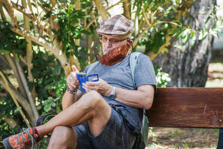 Madrid / Spain - 07 23 20: A man in a bench using his mobile phone at Retiro park using brown face maskのeditorial素材