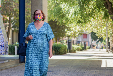 Caceres, Extremadura / Spain - 08 22 2020: retired woman walking on the street and wearing beautiful face mask in summerのeditorial素材