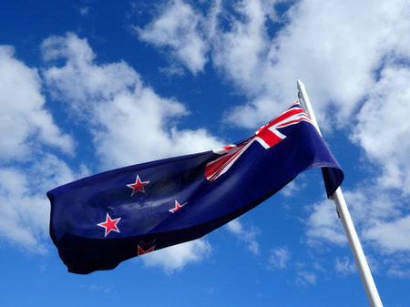 Official New Zealand flag waving in the wind in a sunny blue sky.