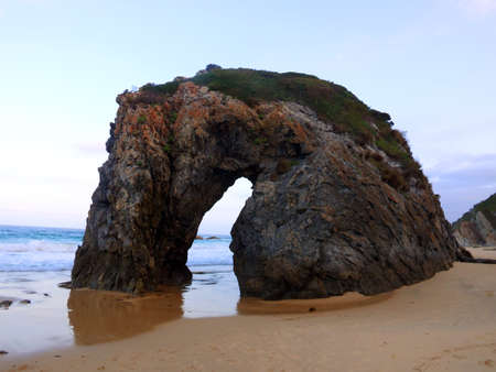 Rock formation gaps on a deserted sandy beach in a clear morningの写真素材