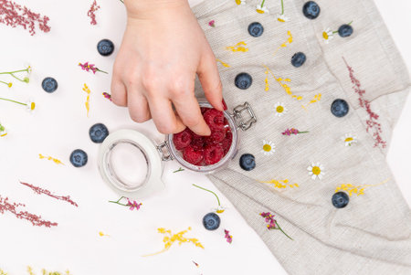 Shot from above of raspberries inside of a jar with a woman's hand picking some, on a pink...