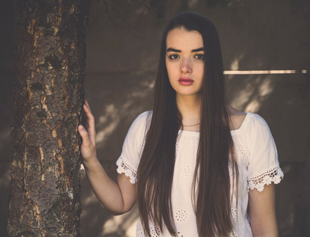 A young girl with long brown hair in a white shirt holding a tree. Looking into the camera.の写真素材