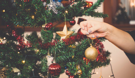 A womans hand decorating a christmas tree.