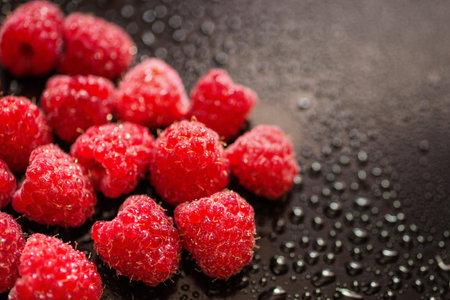 Wet fresh raspberry on black glossy background.