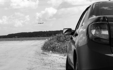 monochrome photo (black and white) car on a gravel road rear view on the background of the plane...