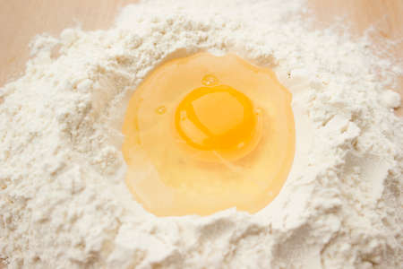 Flour on a wooden cutting board with a egg in the middle of it.の写真素材