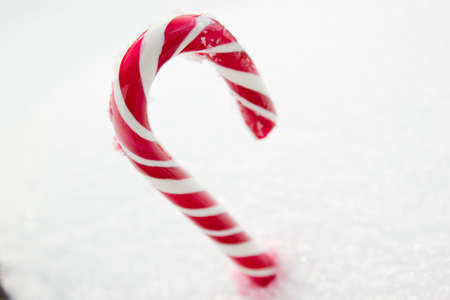 Sweet red and white candy cane lying in the snow.の写真素材