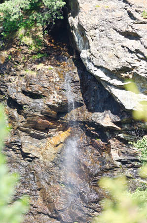 Waterfall in the Alpine mountains with leaves not in focus in the foregroundの写真素材