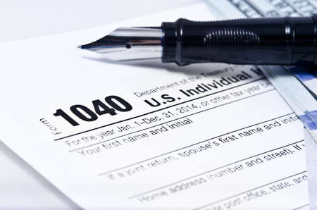 Tax form 1040 on a gray background, blue pen, and 100 dollar bills out of focusの写真素材