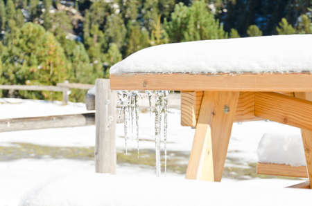 A picnic table covered in snow with an icicle, shallow depth of fieldの写真素材