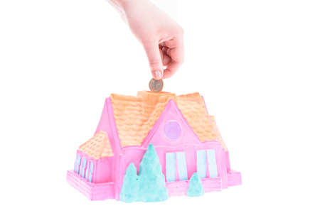 Hand drops a coin into the piggy Bank house on a white background, shallow depth of fieldの写真素材