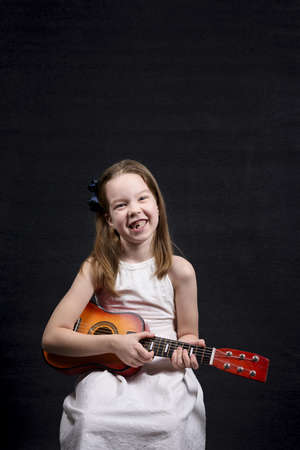 A little girl on a dark background playing a child's guitarの写真素材
