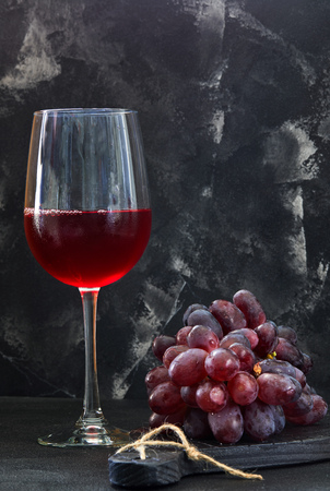 Glass of wine with grapes on a black wooden stand and dark backgroundの写真素材