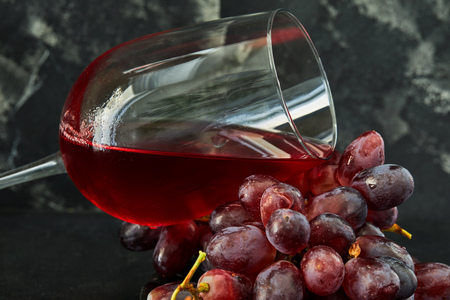 Glass of wine with grapes on a black wooden stand and dark backgroundの写真素材