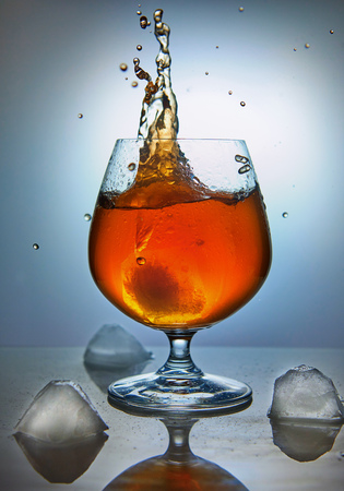 Whiskey, bourbon, brandy or cognac with ice on a blue background. Wave design concept.の写真素材
