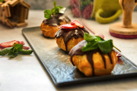 Stack eclair of profiteroles with dark melted chocolate on a black dish. Sprinkle with powdered...