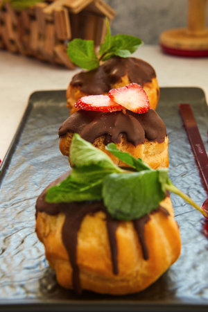 Stack eclair of profiteroles with dark melted chocolate on a black dish. Sprinkle with powdered...
