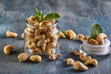 Cashew in a transparent jar with sheets of mint on top on a background with a blue tint.の写真素材