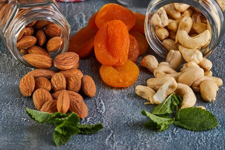 Cashew almonds spill out of transparent cans, dried apricots lie between them against the background with a blue tint.の写真素材