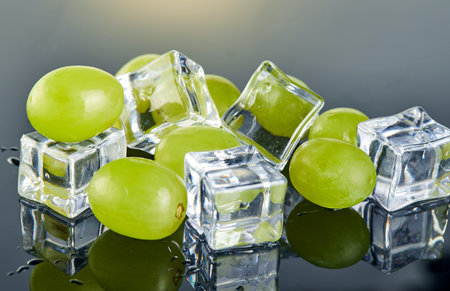 Fresh green grapes with water drops and ice cubes on gray background with reflectionの写真素材