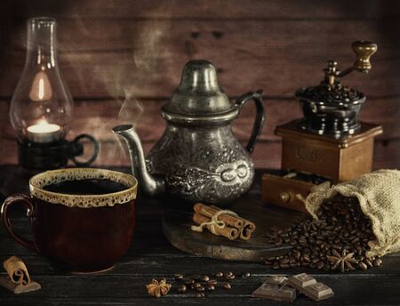 Still life in the style of an old photograph with a coffee grinder, coffee beans with an old lamp and a kettle with a cup with steam.の写真素材