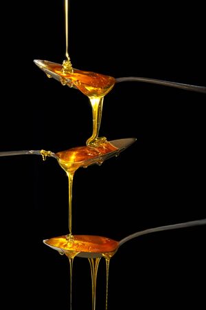 Honey flowing in three spoons from top to bottom on a black background. The concept of movement and healthy eating.の写真素材