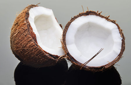 Fresh Coconut chopped into two halves on a gray background with reflection. Vegan organic product.