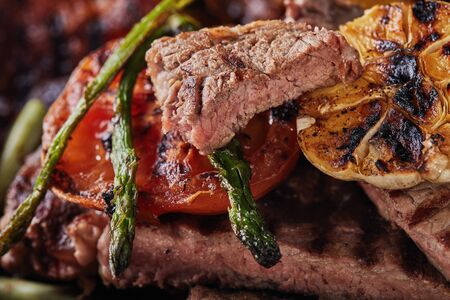 Grilled Beef Steak in a black pan with baked vegetables - tomatoes, asparagus, garlic and peppers. Close-up.の写真素材