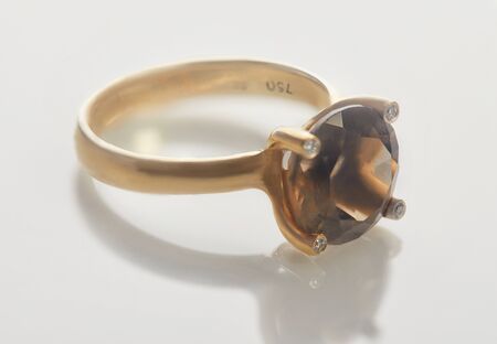Jewelry making. 18k yellow gold ring with diamonds and smok topaz lying on a white background with reflection.の写真素材