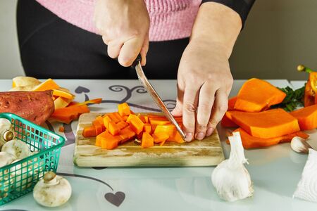Woman slices a pumpkin on a wooden board in the kitchen. Female hands prepare cream soup with pumpkin. Healthy eating concept.の写真素材