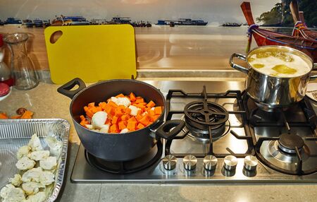 Ingredients for cream soup pumpkin, onions, cauliflower, potatoes, peppers in a pan on a gas stove. Healthy eating concept.の写真素材