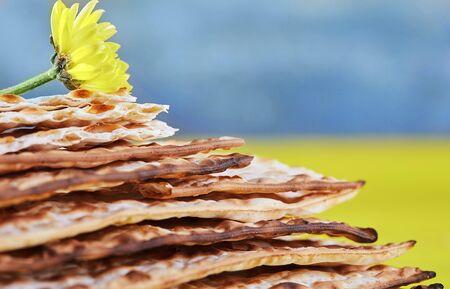 Pesah celebration concept - jewish Passover holiday. A stack of matzo on a yellow-blue background with a yellow flower. Close up. Copy space.の写真素材