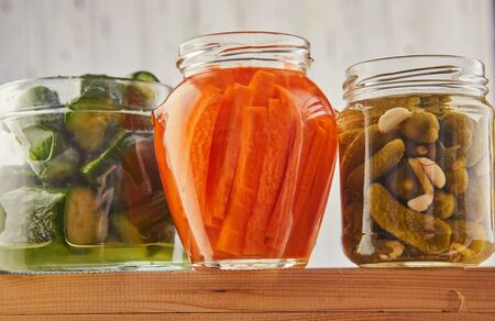 Fermented preserved vegetarian food concept. Pickled carrots, pickled cucumbers, salted cucumbers in glass jars on a wooden kitchen table. The concept of canned food. Copy spaceの写真素材