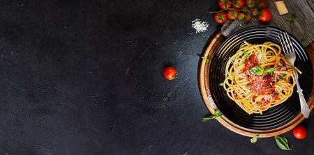 Tasty appetizing classic Italian pasta spaghetti with tomato sauce, parmesan and basil on a plate on a dark table. Top view, horizontal. Flat lay. Copy space. Bannerの写真素材