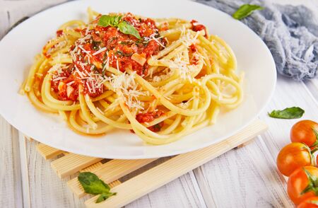 Tasty appetizing classic Italian spaghetti pasta with tomato sauce, parmesan and basil on a plate on a light wooden background. Side view. Copy space close-upの写真素材